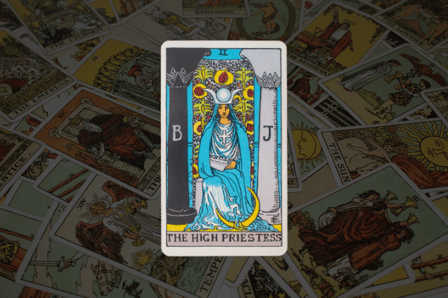 Na imagem, há a carta A Sacerdotisa do Tarot na posição normal. Ao fundo, há várias cartas de Tarot.