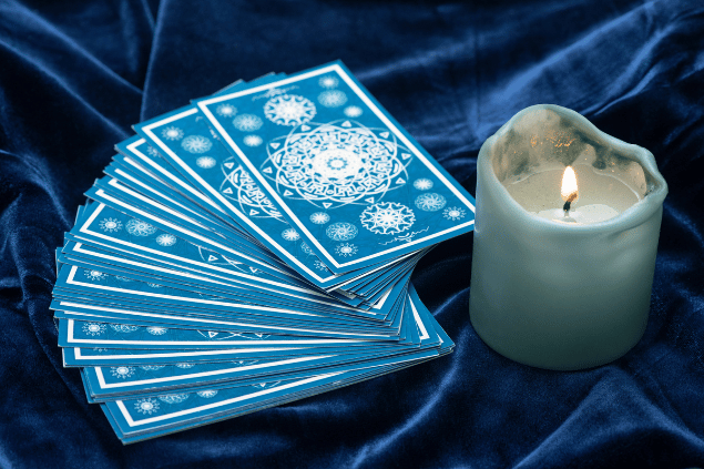 Várias cartas de Tarot estão dispostas sobre uma mesa. Ao lado, há uma vela.
