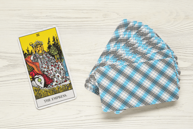 A carta A Imperatriz do Tarot e um baralho com outras cartas virado para baixo estão sobre uma mesa de madeira.