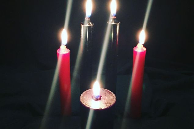 Imagem de algumas velas de cores escuras acesas, simbolizando um dos itens de oferendas para o Exu da Meia-Noite.