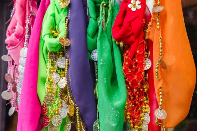 Imagem de vários lenços coloridos e decorados com miçangas e medalhas nas cores dourada e prateada, simbolizando um dos adornos da pombagira Dama da Noite.