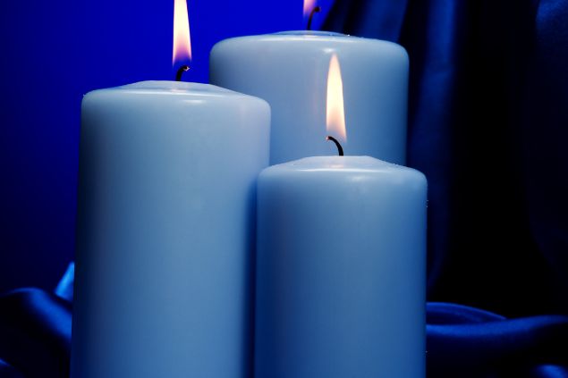Imagem de três velas grandes e acesas na cor azul claro, simbolizando uma das oferendas para o Cigano Igor da Umbanda.