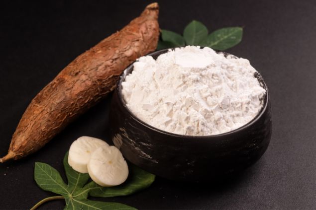 Imagem de um bowl contendo farinha de mandioca. Ao lado, uma mandioca com casca, folhas do legume, completam os elementos da foto, simbolizando uma das oferendas para o Exu Gato Preto.