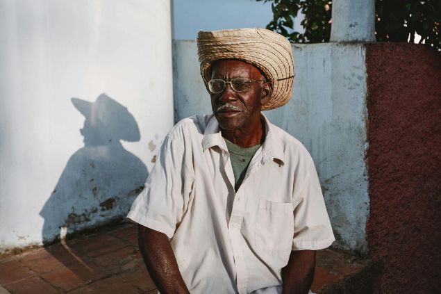 Imagem de um homem idoso, negro, usando uma camisa branca e um chapéu na cabeça, simbolizando o Pai João na Umbanda.