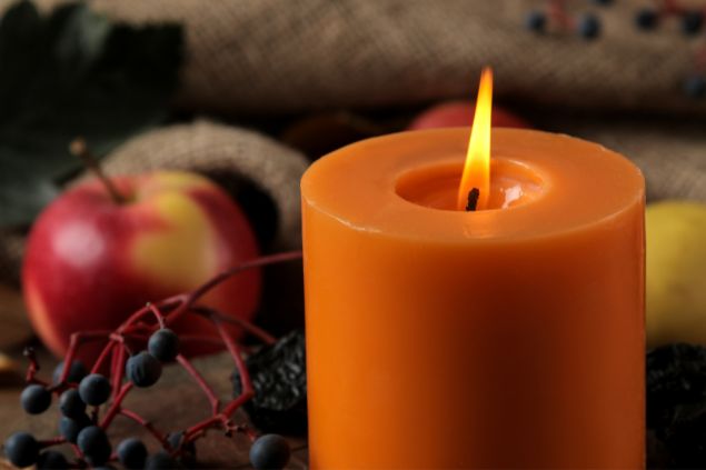 Imagem de uma vela na cor laranja e vários tipos de frutas, simbolizando uma oferenda para a orixá Egunitá da Umbanda.