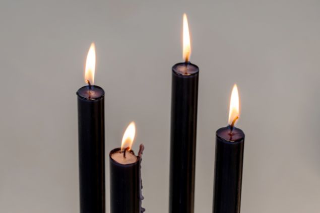 Imagem de quatro velas pretas acesas, simbolizando uma oferenda para o Exu Lalu da Umbanda.