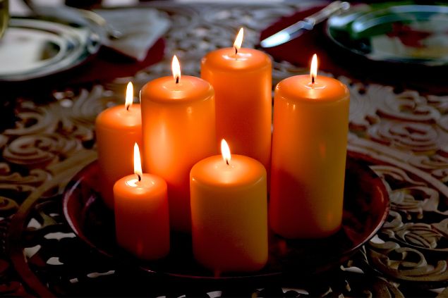 Imagem de seis velas acesas na cor laranja, simbolizando uma oferenda para o Exu Gira Mundo da Umbanda.