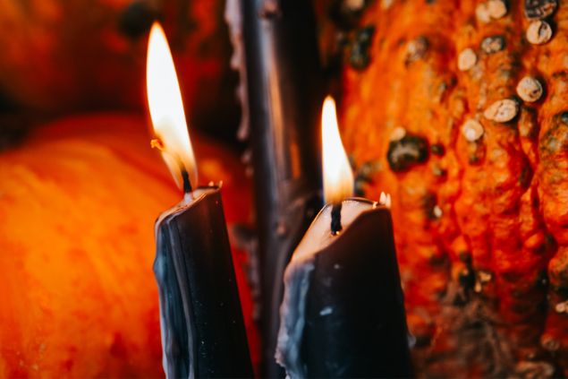 Imagem de fundo vermelho e em destaque duas velas acesas na cor preta, simbolizando uma oferenda para o Exu 7 Encruzilhadas.