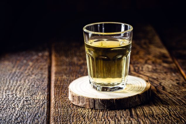 Imagem de um copo com dose de pinga sobre uma mesa de madeira, simbolizando uma das oferendas para o Exu Tatá Caveira.