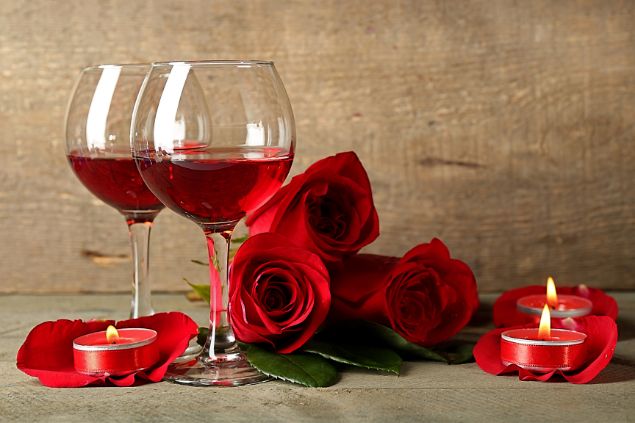 Imagem de duas taças de vinho, rosas e velas vermelhas acesas, simbolizando uma das oferendas para a Pombagira Rosa Negra da Umbanda.