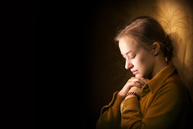 Imagem de uma mulher encostada em uma parede fazendo a sua oração para Oxalá.