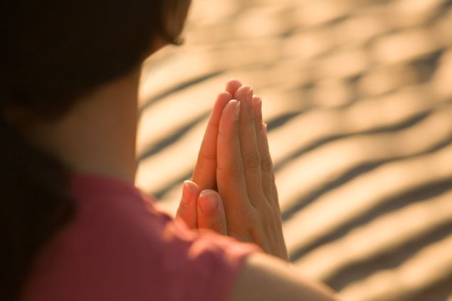 Imagem de uma mulher em pé, fazendo a sua oração. 