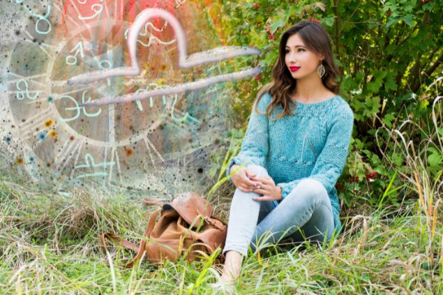 Imagem de uma mulher usando uma blusa azul e uma calça jeans, sentada em um gramado e ao lado, o glifo do signo de Libra.