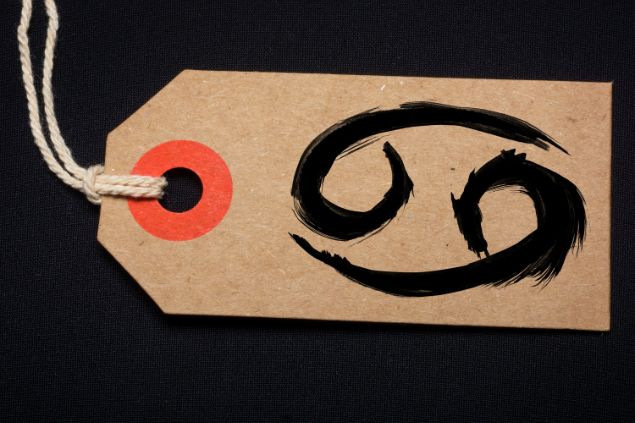 Imagem de fundo preto e em destaque uma etiqueta com o glifo de câncer.