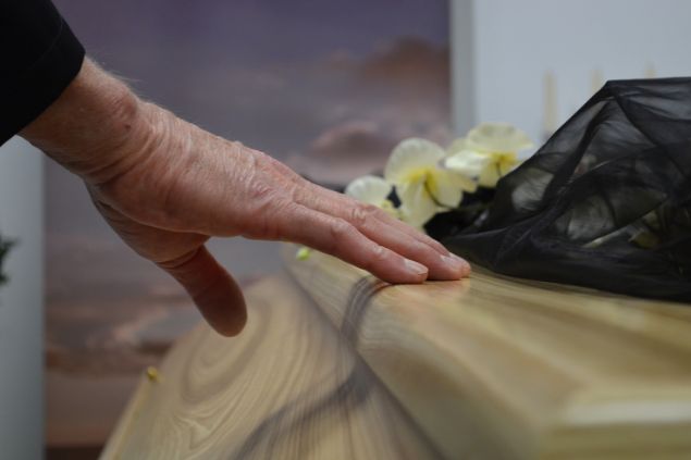 Imagem de uma pessoa tocando um caixão de madeira de um parente que faleceu.