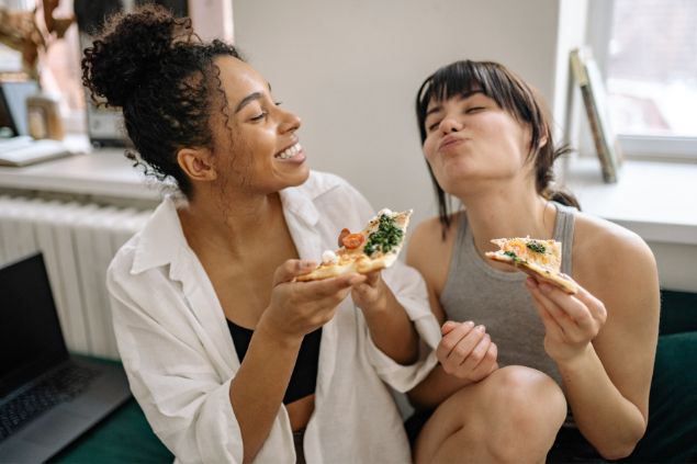 Imagem de duas moças jovens comendo pizza com as mãos, representando o signo de touro.