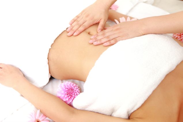 Imagem de mulher no início da gravidez, recebendo uma massagem shiatsu na barriga.