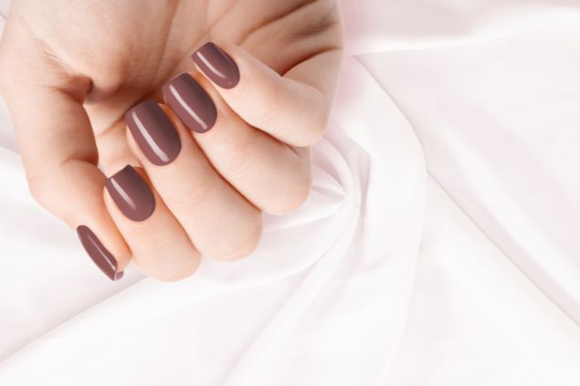 Imagem de uma mão com as unhas pintadas na cor chocolate.