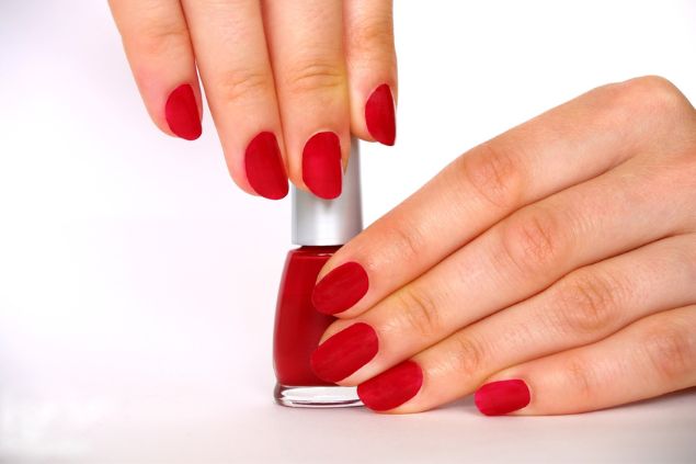 Imagem das mãos de uma mulher com as unhas pintadas na cor de vermelho fechado.