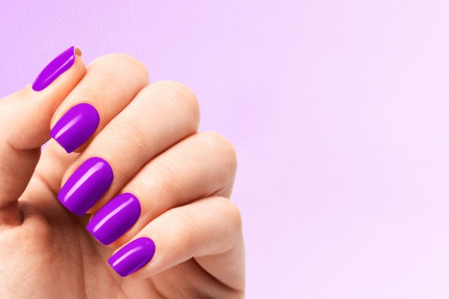 Imagem da mão de uma mulher com as unhas pintadas na cor violeta.