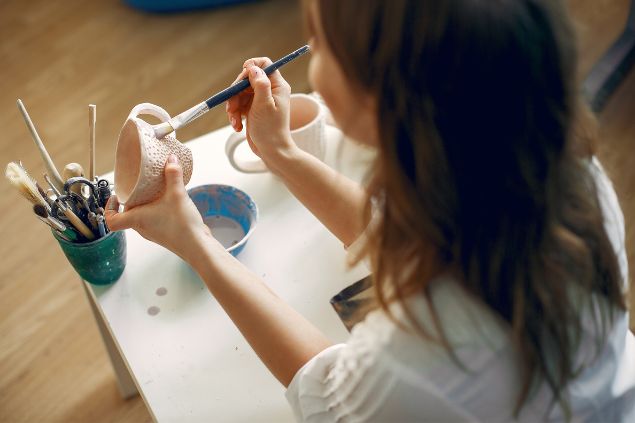 Imagem de uma artesã pintando peças de argila na mesa, uma das habilidades do signo de sagitário.