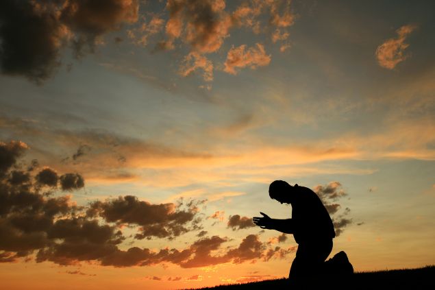 Imagem de um lindo pôr do sol e em destaque a silhueta de um homem de joelhos fazendo a sua oração.