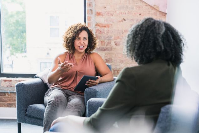 Imagem de duas pessoas sentadas em um sofá em uma sala de estar. Elas estão trocando conselhos e uma delas é a líder emocional.