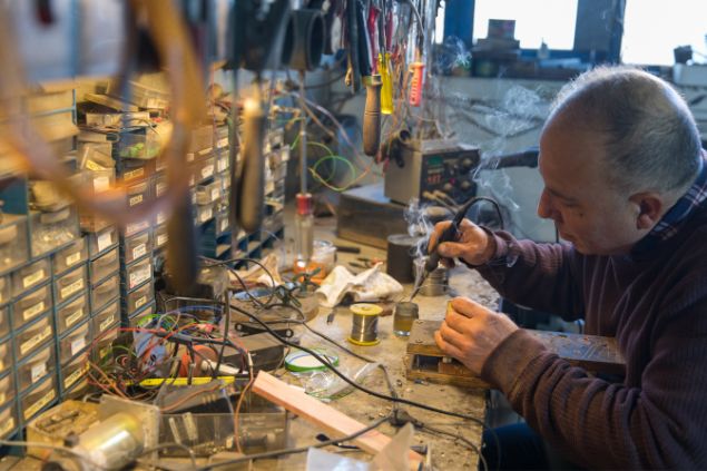 Imagem de um inventor soldando algumas peças sobre uma mesa de trabalho.