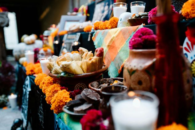 Imagem de um altar com flores, alimentos, velas, tecidos e comidas que formam um santuário feito para as oferendas.