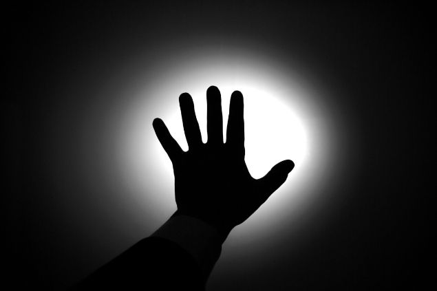 Imagem em preto e branco e em destaque uma mão sobre uma luz. A foto traz o conceito de vida após a morte.