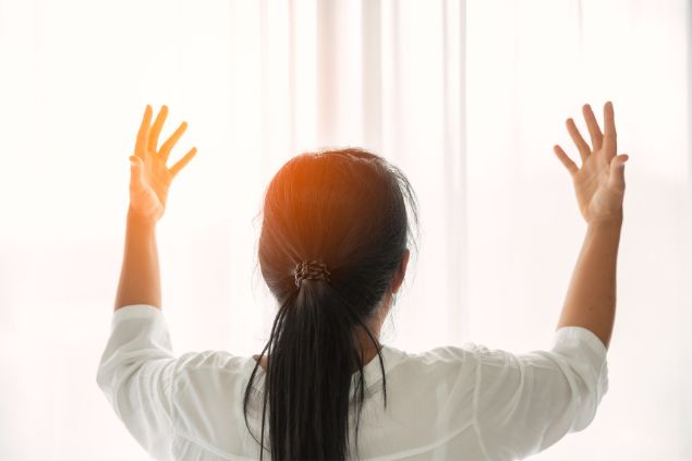 Imagem de uma mulher com as mãos erguidas recebendo um passe espiritual vindo da energia solar.