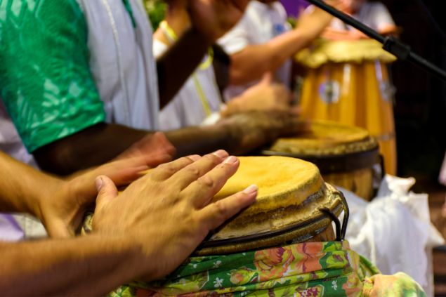 Imagem de um terreiro de umbanda. Os filhos tocam vários instrumentos, como o atabaque.