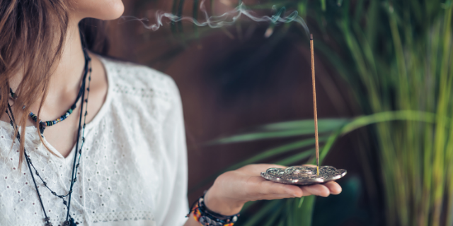 Mulher segura incensário; sobre ele, há um incenso aceso. 