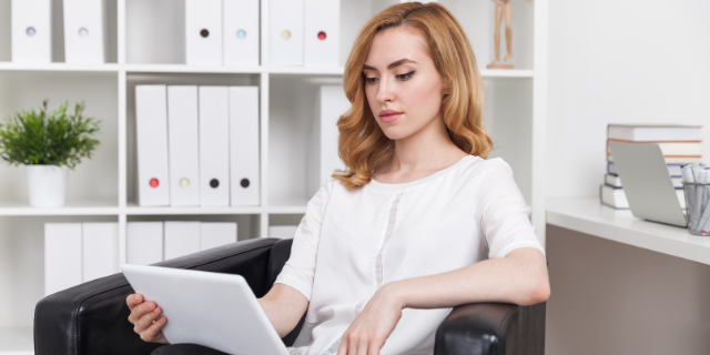 Mulher sentada com um tablet em mãos.