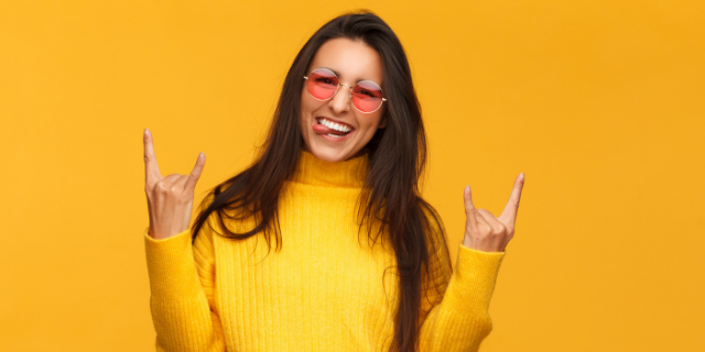 Mulher sorrindo e com as mãos chifradas erguidas.