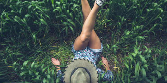Mulher deitada sobre grama com as pernas cruzadas e erguidas.