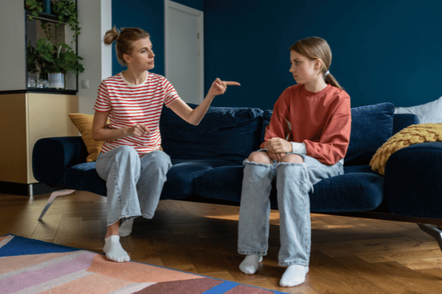 Mãe e filha sentadas no sofá. A mãe está dando uma bronca enquanto aponta o dedo. 