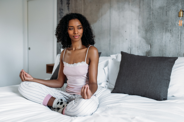 Mulher sentada na cama em posição de lótus olhando para o lado