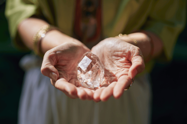 Uma mulher está com as mãos juntas segurando um cristal transparente.