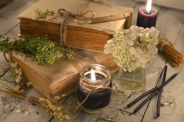 Vera Petruk / Canva Na imagem, há alguns recipientes com flores e velas em cima de uma mesa. Há dois livros também.