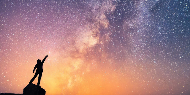 Pessoa em cima de uma pedra apontando para o céu estrelado