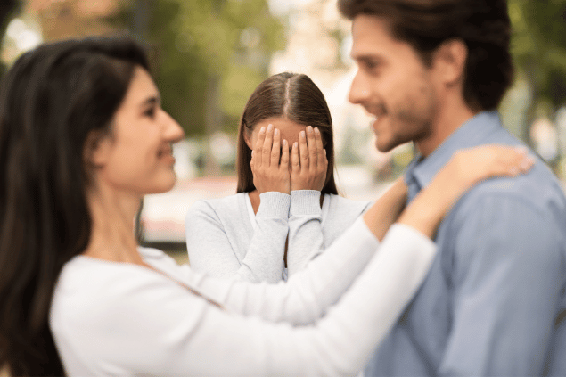 Mulher chorando com as mãos no rosto ao ver seu parceiro com outra mulher. 