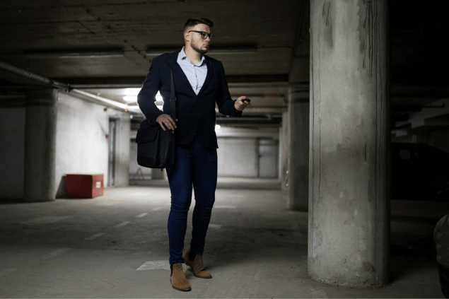 Homem branco vestido de terno tentando procurar seu carro em um estacionamento. 