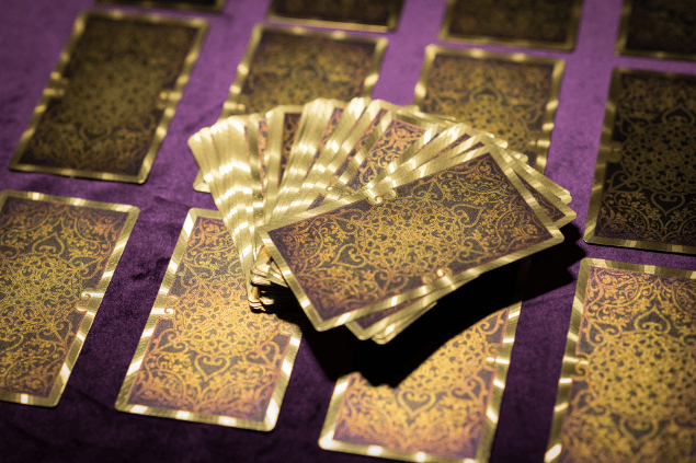 Várias cartas de Tarot estão dispostas sobre uma mesa. Há um baralho centralizado na imagem.