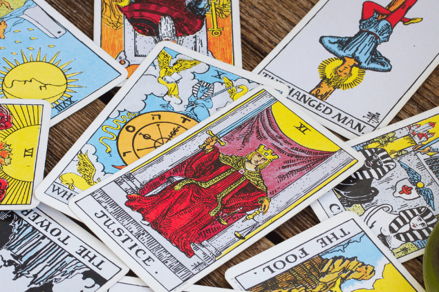 Há várias cartas de Tarot espalhadas sobre uma mesa de madeira. A carta A Justiça está em destaque.