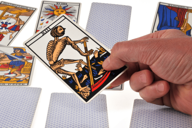 Uma pessoa segura a carta A Morte do Tarot que está em destaque na imagem. Embaixo dela, há outras cartas.