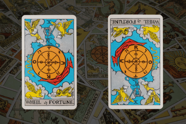 Montagem com a carta A Roda da Fortuna do Tarot na posição normal e outra carta A Roda da Fortuna na posição invertida. Ao fundo, há várias cartas de Tarot.
