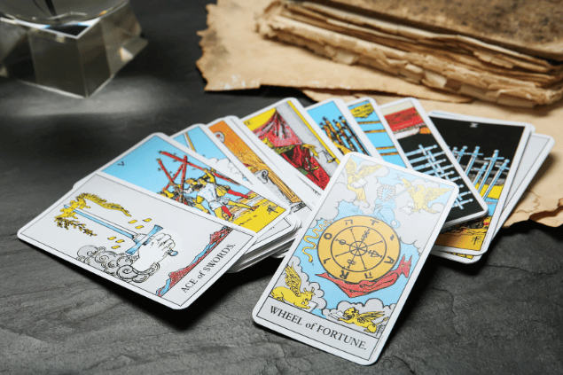A carta A Roda da Fortuna do Tarot está em destaque sobre uma mesa de pedra. Ao lado, há outras cartas de Tarot.
