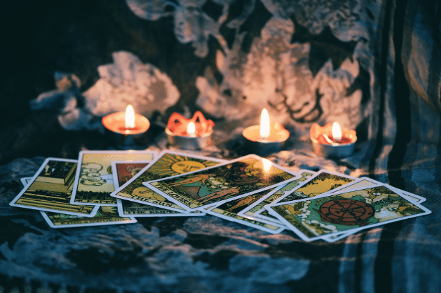 Várias cartas de Tarot estão espalhadas sobre uma mesa. Há velas acesas ao lado.