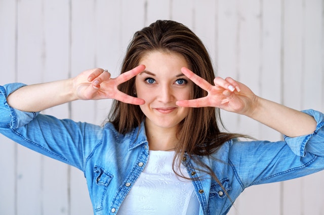 Mulher com mãos fazendo o número dois em frente aos olhos sorrindo